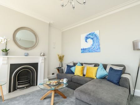 A living room with a grey sofa with colorful cushions a glass coffee table and a fireplace at Ocean Retreat in Weymouth