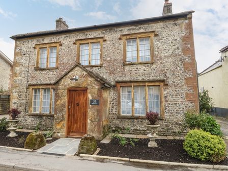 Stone house with wooden door and four windows and plants in front at Norden House in Maiden Newton