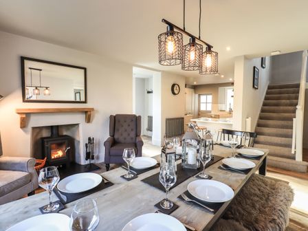 A dining area with a wooden table set with plates and glasses next to a living area with armchairs and a fireplace at Raybarrow in Windermere