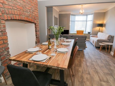 A dining area with a wooden table set for six people and a living room with sofas and a yellow chair at Hilderthorpe House in Bridlington