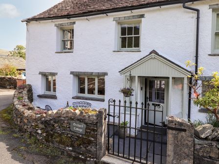 The exterior of Orchard Cottage with white walls stone fence metal gate and outdoor seating area in Troutbeck