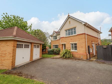 A two-story house with brick and cream walls next to a detached double garage with white doors and a driveway at Pencraig in Rhos-On-Sea
