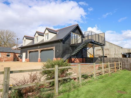A two-story building with garage doors and an external staircase with a railing in a rural setting at The Attic in Blackborough End near Kings Lynn
