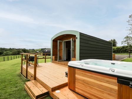 An outdoor deck area with wooden steps a hot tub and a small cabin with open doors at Hwyl in Rhayader near Llandrindod Wells