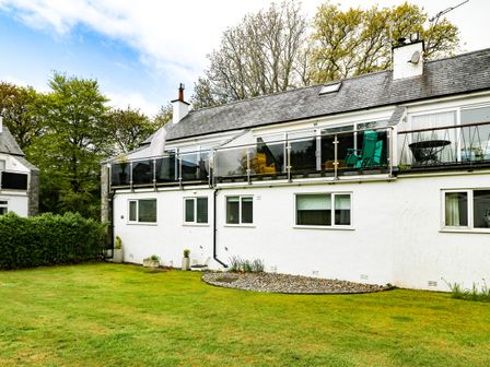 A white building with upper balconies and green chairs on a lawn at 22 Glyn Y Mor in Llanbedrog