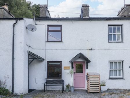 A white exterior of a cottage with a pink door a black bench and potted plants at Turn Cottage in Satterthwaite near Hawkshead