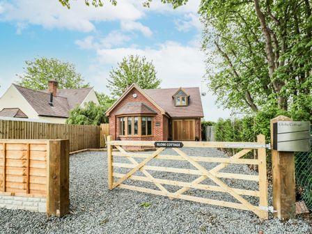 A front yard with a wooden gate and gravel driveway leading to a brick house at Globe Cottage Stratford-Upon-Avon