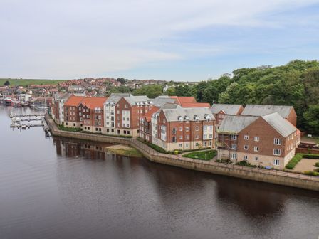 A row of residential buildings along a river with a marina and houses in the background at Heron's Landing in Whitby