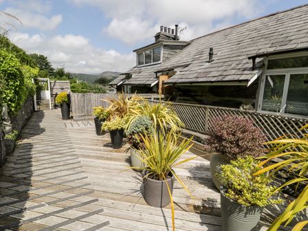 An outdoor wooden deck with multiple potted plants beside a house with a slate roof at The Sail Loft in Porthmadog