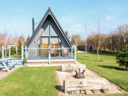 A gray A-frame cabin with a deck and outdoor seating in a grassy yard at Silver Birch Lodge in Misterton
