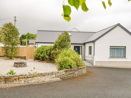 Exterior of a white house with a gray roof a gravel area with a circular stone feature and greenery at Wee Andys in Slavary near Buncrana County Donegal