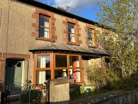 Exterior view of a two-story house with brown framed windows and a green front door at 2 West View in Allithwaite near Grange-over-Sands