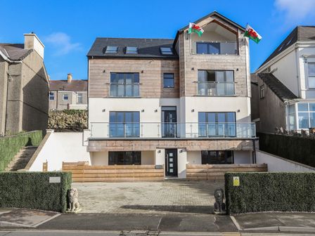 A modern three-story house with balconies and glass railings between two other buildings at Bryn Min Manton Apartment in Caernarfon