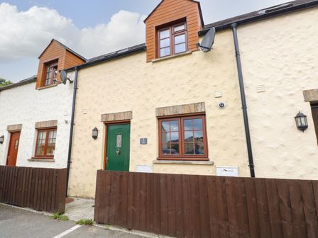 Exterior view of a beige terraced house with green door brown wooden fence and windows at Bwthyn Canol in Haverfordwest