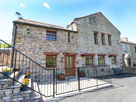 Exterior stone wall of a house with wooden framed windows and door with metal gate and stone steps with flowers at Birkett Barn in Kirkby Stephen