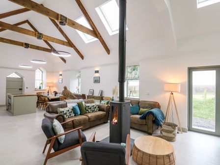 An open plan living and dining area with exposed wooden beams wood burning stove and dining table at Ysgoldy Brynwyre in Llanrhystud