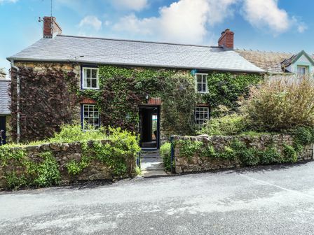 A stone house covered with ivy with two chimneys and a small stone wall in front at Tyddyn Bach Newport Pembrokeshire