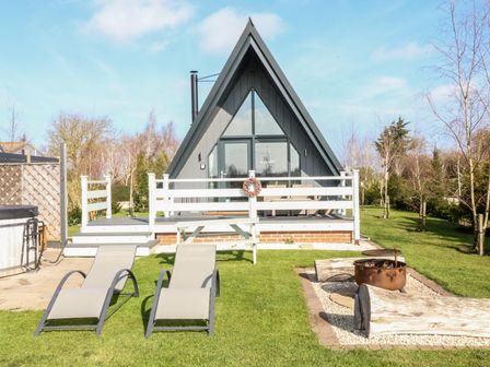 A small A-frame cabin with a porch two lounge chairs a picnic bench and a fire pit in the garden at Buttercup Lodge in Misterton