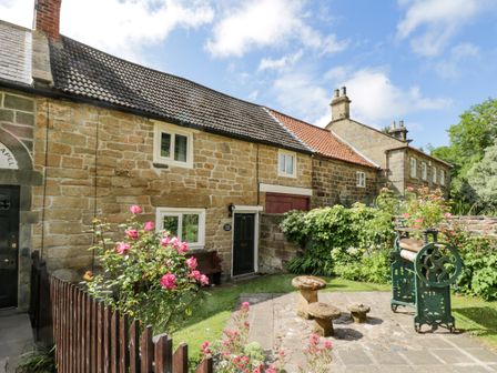 A stone cottage with flower bushes and garden equipment in a courtyard at Chapel Cottage in Upleatham near Saltburn-By-The-Sea