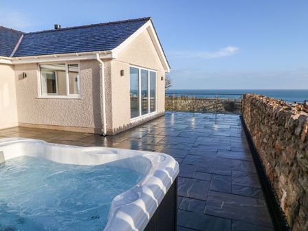 An outdoor patio with a hot tub stone wall and sea view at Yr Hen Feudy in Moelfre