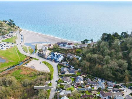 An aerial view of a coastal village with houses roads trees and a beach at By The Beach in Seaton Cornwall