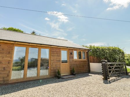 A wooden building with large glass doors and a small window beside a gravel driveway with a wooden gate at FAIRFIELD in Clee Hill
