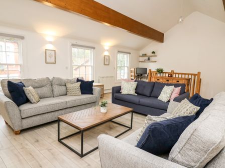 A living room with three sofas around a wooden coffee table and a wooden beam on the ceiling at Bridgend Cottages in Howey near Llandrindod Wells