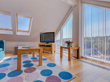 A living room with wooden tables a TV and a rug with colorful circles at The Penthouse in St Ives