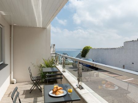 A balcony with two tables and chairs overlooking a street and the sea with croissants and orange juice on one table at The Point in St Ives