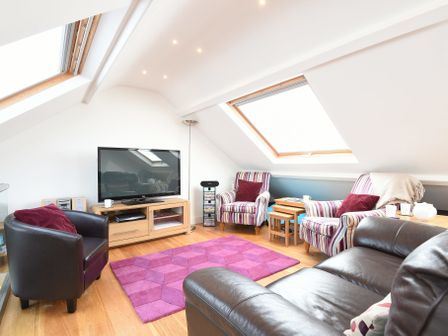 A living room with leather and striped armchairs a television on a wooden stand and skylight windows at The Sail Loft in St Ives