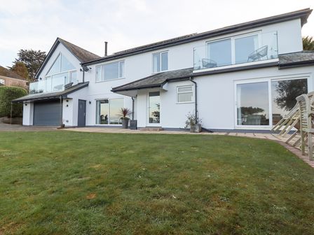 A two-story house with glass balconies lawn and outdoor chairs at Treetops in Carbis Bay