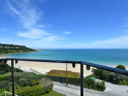 A beach with sand and people by the sea viewed from a balcony with railing at Treth Ha Mor in Carbis Bay