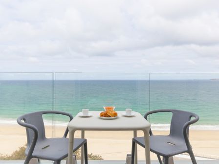 A balcony with a table set with cups and pastries overlooking the sea at Turquarze Carbis Bay