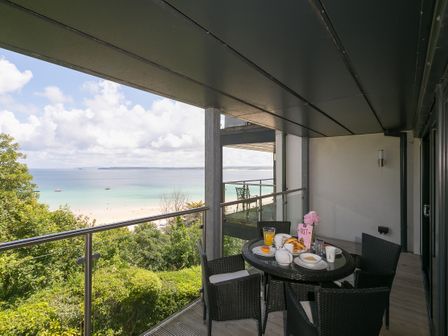 A balcony with a round table set for breakfast and four chairs overlooking a beach and ocean at Waters Edge in St Ives