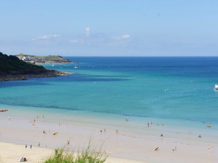 A beach with people in the water and on the sand with boats in the sea at Waves in Carbis Bay