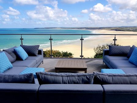 An outdoor seating area with grey sofas and blue cushions overlooking a beach and ocean at Whitsunday House in Carbis Bay