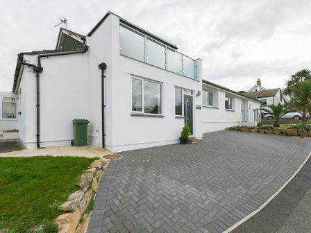 A white house with a paved driveway and glass balcony at Sanctuary Bay in Carbis Bay
