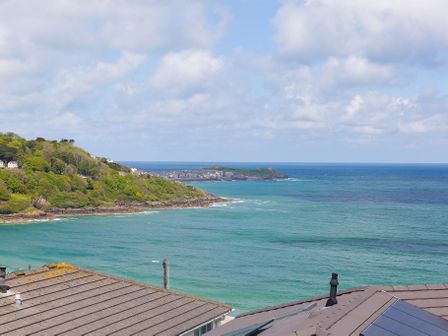 A coastal view of the sea with a green hill on the left and rooftops in the foreground at Gwel An Chapel in Carbis Bay