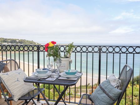 A balcony with a table set for two with bowls glasses and a vase of flowers overlooking a beach and the ocean at Blue Horizons in Carbis Bay