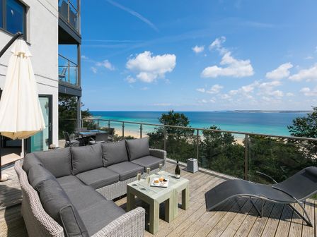 An outdoor terrace with a sectional sofa table and lounge chair overlooking the beach at 4shore in St Ives