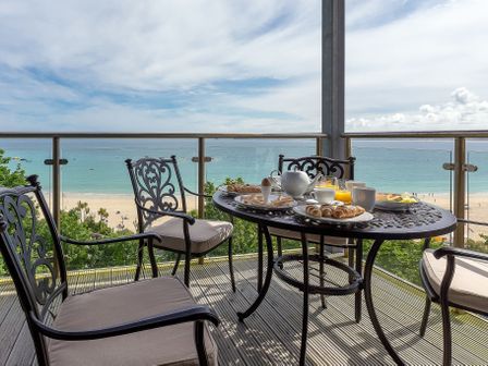 A patio table with breakfast items and chairs overlooking a beach and ocean at Abalone in St Ives