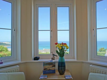 Three large windows overlooking the sea with flowers in a vase on a table underneath at Amethyst in Carbis Bay