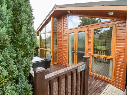 A wooden lodge exterior with glass doors and windows and outdoor seating at Oak Lodge in Glasshouse