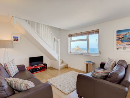 A living room with two brown leather sofas a white rug a small wooden table and a view of the sea at Atlantic Blue Carbis Bay