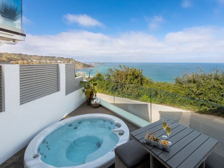 A balcony with a hot tub a table with drinks and snacks and a view of the ocean at Atlantic Watch 8 in Carbis Bay