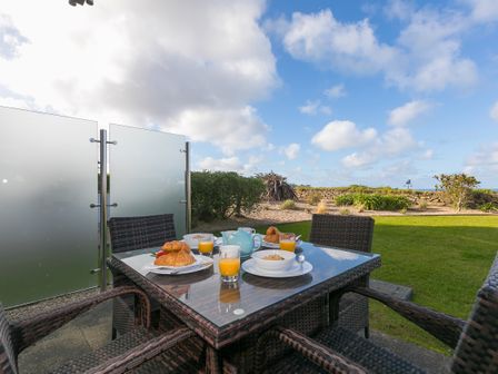 An outdoor patio table with four wicker chairs set with breakfast bowls croissants orange juice and a teapot at Beach Haven in Carbis Bay