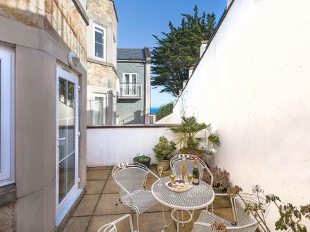 A small outdoor patio with a round metal table and metal chairs with glasses and a bottle on the table and potted plants along the walls at Beach Retreat in Carbis Bay