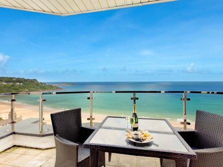 A balcony with a glass table and two chairs overlooking the ocean at Blue Vista in Carbis Bay