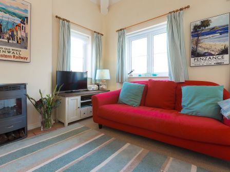 A living room with red sofa blue cushions TV and striped rug at Brinyloft in Carbis Bay