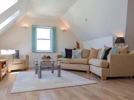 A living room with a beige sectional sofa and armchair a glass coffee table and a window with blue shutters at Celeste in Carbis Bay